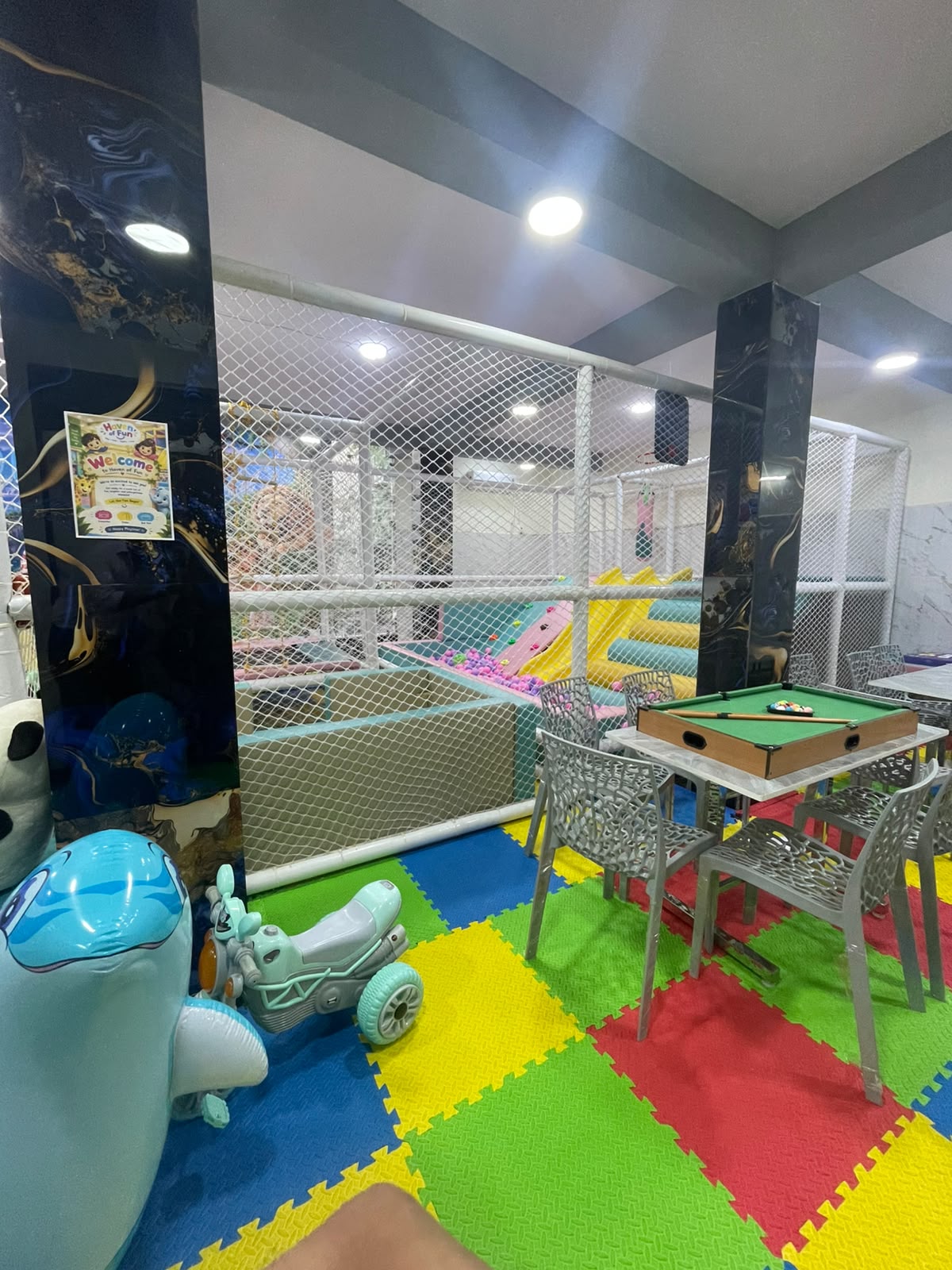 A colorful indoor playground with a ball pit, slides, and seating area for children.