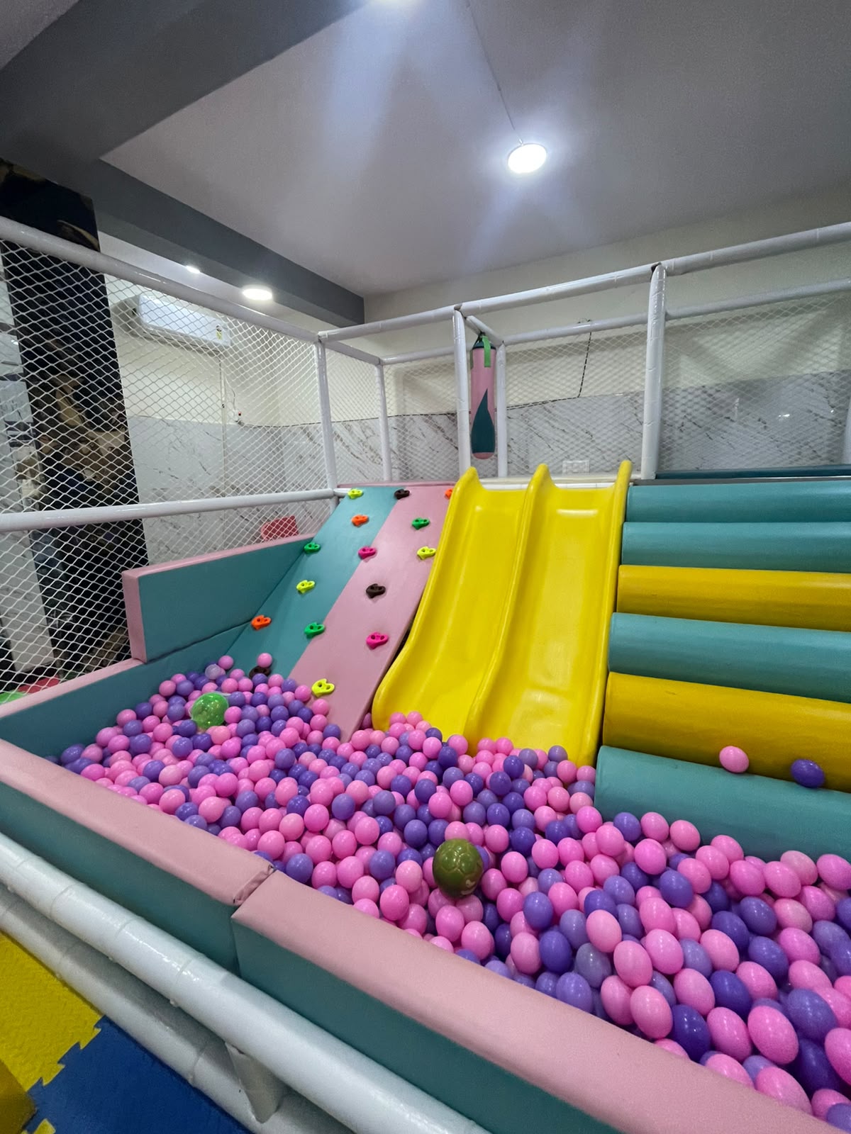 A colorful indoor playground with a ball pit, slides, and climbing wall for children.