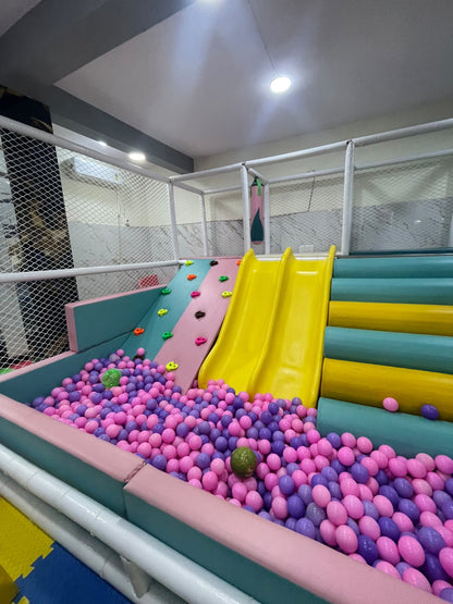 A colorful indoor playground with a ball pit, slides, and climbing wall for children.