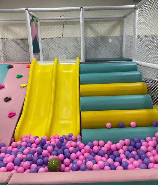 A colorful indoor playground with slides, ball pit, and climbing wall for children.