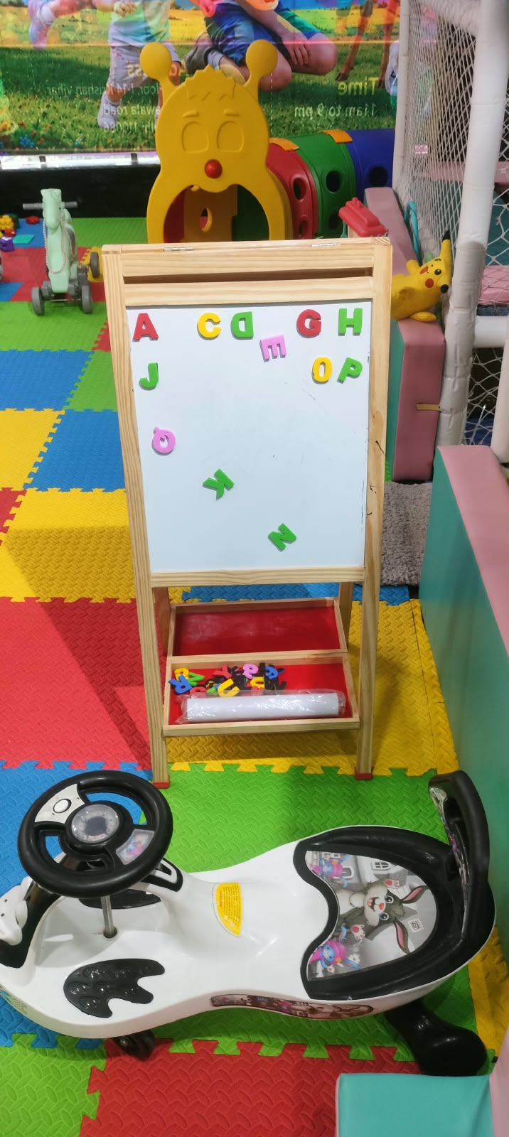 A child's play area with a whiteboard, toy car, and colorful floor mats.