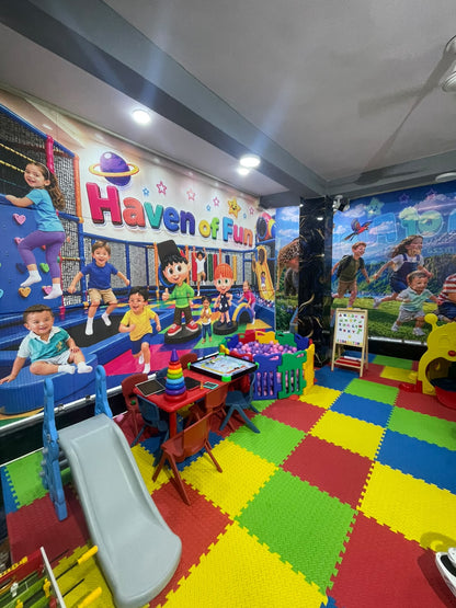 A colorful indoor playground with children playing, featuring a climbing wall, ball pit, and tables.