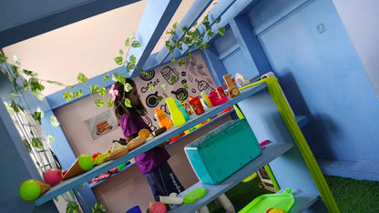 A young girl plays at a toy cafe with colorful food items and a turquoise cash register.