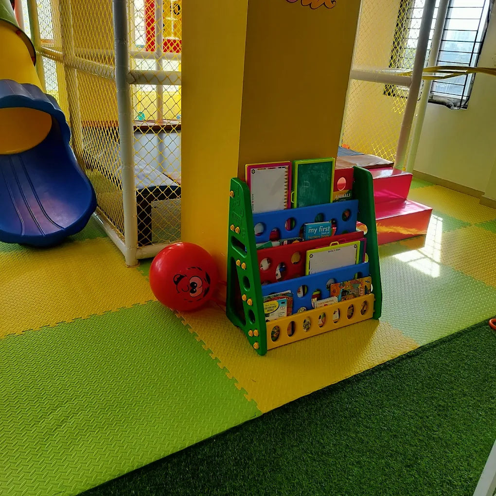 A colorful indoor playground with a slide, ball, and bookshelf filled with children's books.
