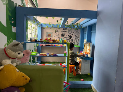 A young child plays at a toy kitchen in a colorful playroom with stuffed animals.