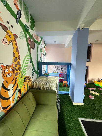 A brightly decorated playroom with a jungle theme, featuring a green couch, artificial grass, and a play structure.