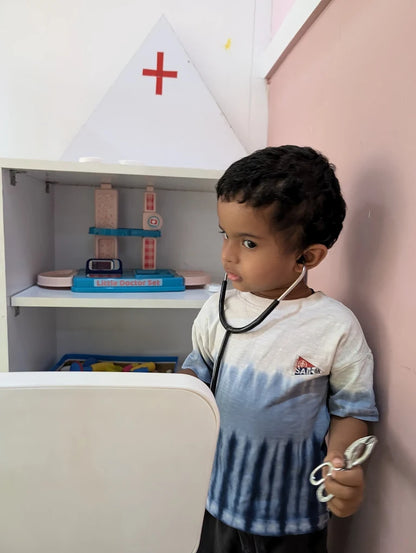 A young child plays doctor with a stethoscope and toy medical tools in a room with a toy doctor set.