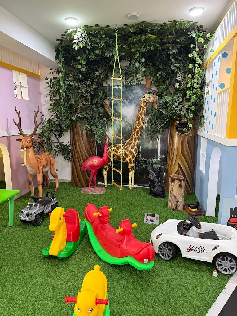 A playful indoor jungle-themed play area with animal figures, rocking toys, and a ride-on car for young children.