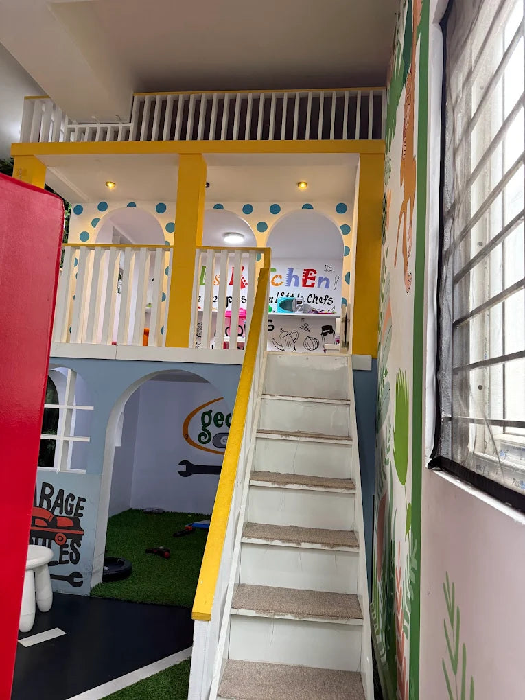 A colorful indoor playhouse with a kitchen and garage theme, featuring a staircase and playful decor.