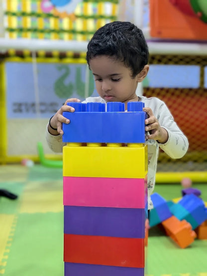 A young child stacks colorful oversized building blocks in a playroom.