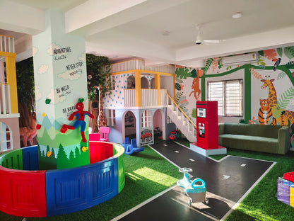 A colorful indoor playground with a jungle theme, featuring a climbing structure, a ball pit, and animal murals.