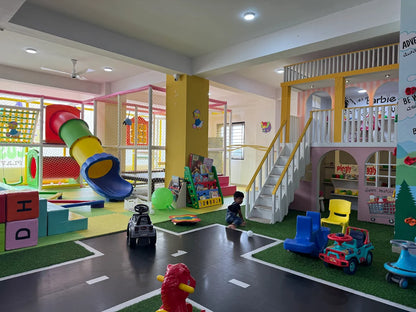 A young child plays in a colorful indoor playground with slides, climbing structures, and toy cars.