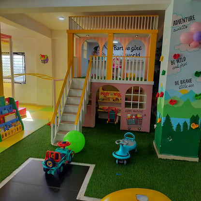 A colorful indoor playground with a playhouse, climbing wall, and toys for young children.
