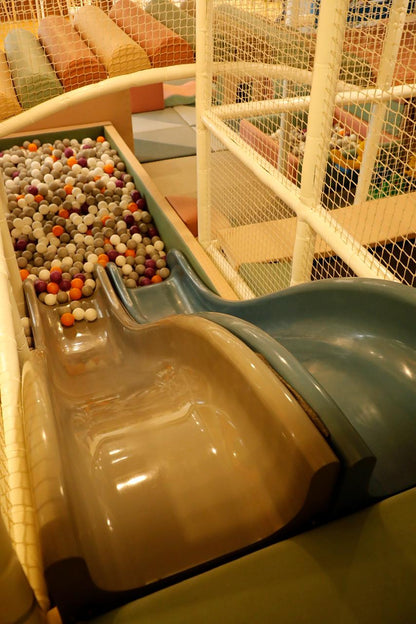 Two slides descend into a ball pit filled with colorful balls, at a children's indoor playground.