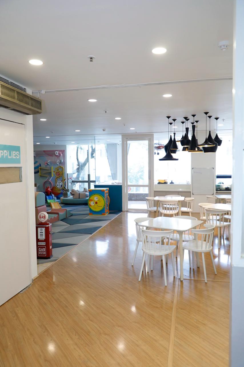 A bright, modern play area with tables and chairs for children, featuring a colorful play structure and decorative gas pumps.