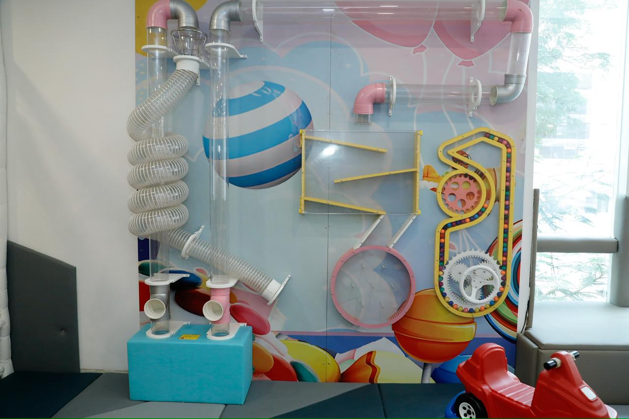 A colorful indoor play area with tubes, gears, and a ball run for children.