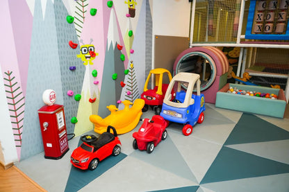 A colorful indoor playground with ride-on toys and a ball pit for young children.