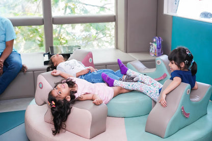 Three young girls relax on colorful, cushioned seating in a bright room.