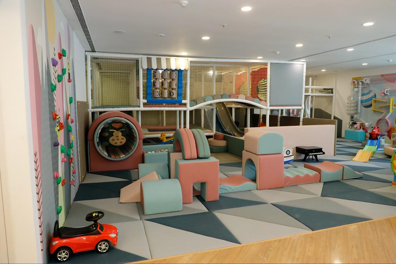 A colorful indoor playground with soft play structures, slides, and a climbing wall for young children.