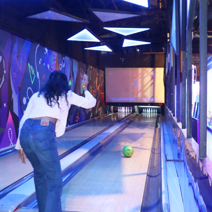 A young person bowls in a neon-lit bowling alley.