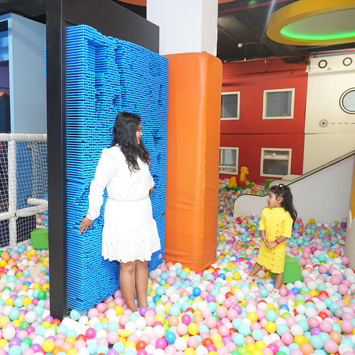 A woman and a young child play in a ball pit at an indoor playground.