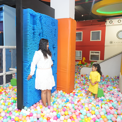 A woman and a young child play in a ball pit at an indoor playground.