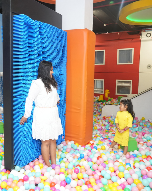 A woman and a young girl play in a ball pit next to a large blue pin art sculpture.