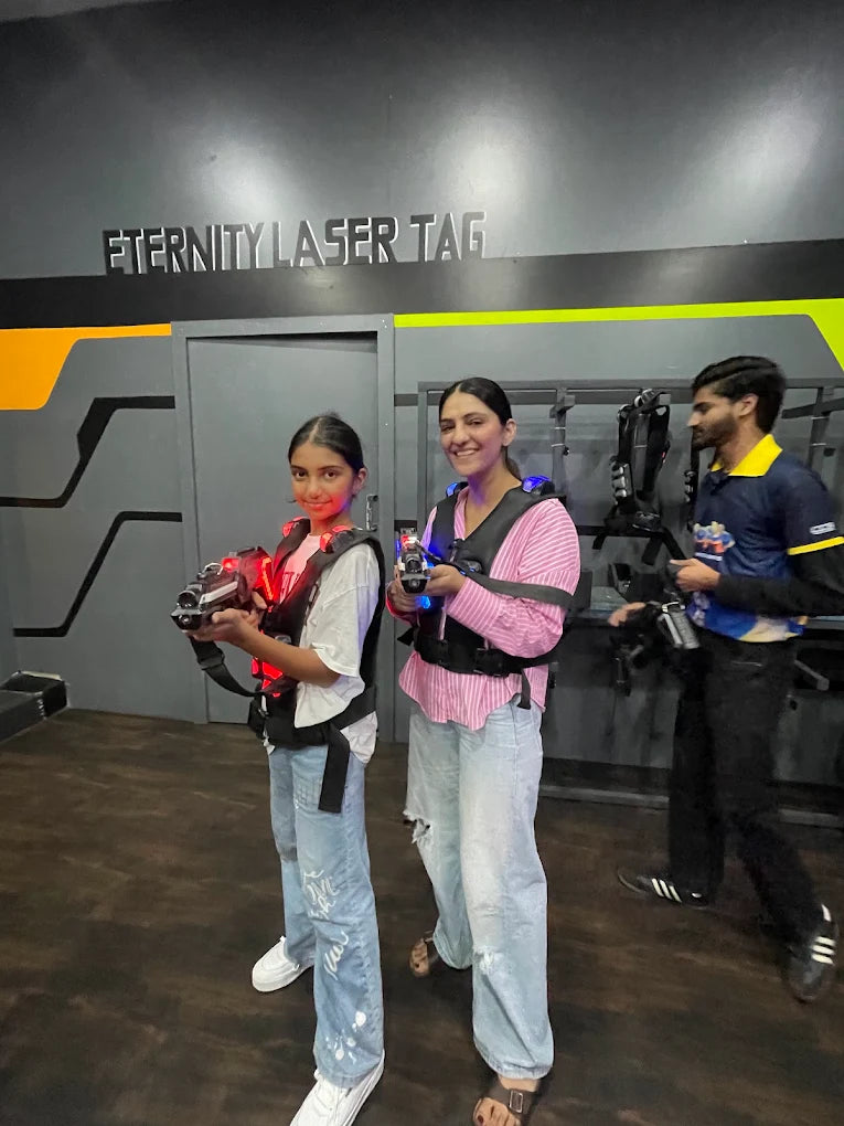 Two young people and an adult play laser tag in a dark arena.
