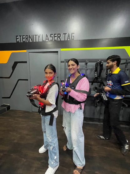 Two young people and an adult play laser tag in a dark arena.