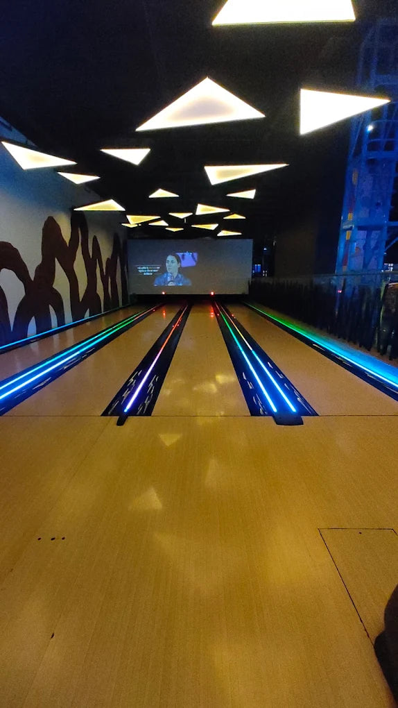 A bowling alley with illuminated lanes and a screen showing a person.