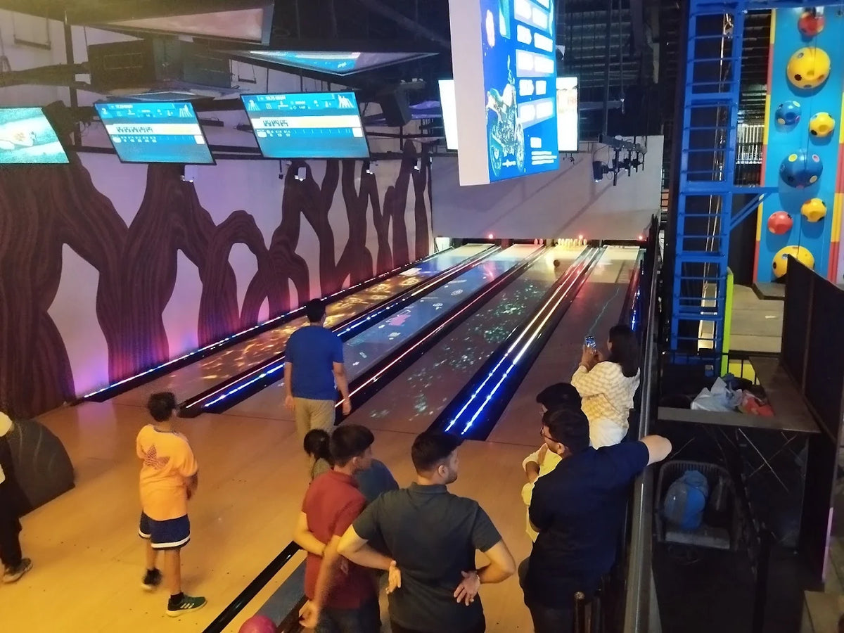 People of various ages bowl at a brightly lit entertainment center with a climbing wall.