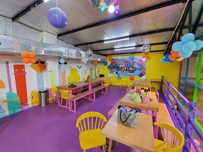 Bright party room with colorful decorations, tables, yellow chairs, and a vibrant birthday banner on the wall