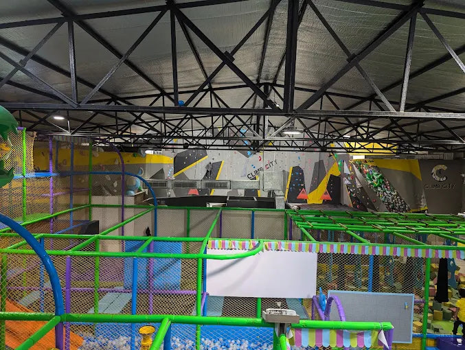 Indoor playzone featuring climbing walls, ball pits, and colorful padded structures with safety netting and soft flooring