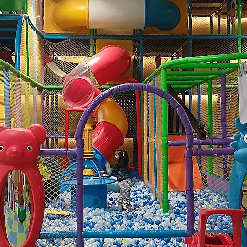 Indoor play area with colorful climbing tubes, ball pit filled with white and blue balls, and soft padded structures