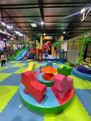 Indoor play space with soft foam flooring, colorful slides, climbing frames, and rotating animal-shaped seats