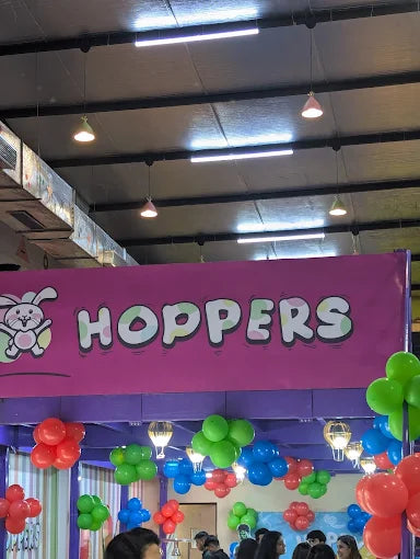 Indoor play area entrance with colorful balloons and a bright pink banner displaying a playful bunny logo and HOPPERS name