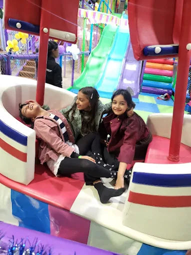 Three smiling children playing together on a colorful amusement ride inside a lively indoor play area