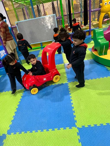 Toddlers playing with a red toy car and exploring colorful climbing equipment on a soft padded playfloor