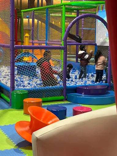 Children playing inside a colorful ball pit and climbing structure in a vibrant indoor play space with soft flooring