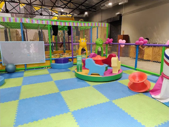 Colorful indoor play area with soft interlocking foam tiles, animal-shaped climbing structures, and fenced safety netting