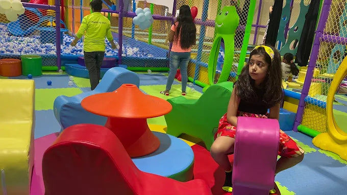Indoor playroom with soft foam play structures, colorful seating, and children exploring a fenced activity area