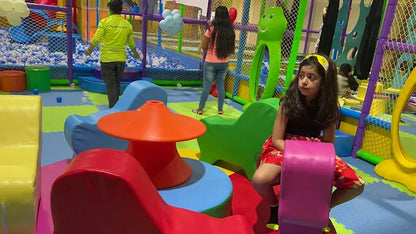 Indoor playroom with soft foam play structures, colorful seating, and children exploring a fenced activity area