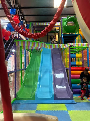 Indoor playground with three colorful slides side by side and soft interlocking foam flooring underneath