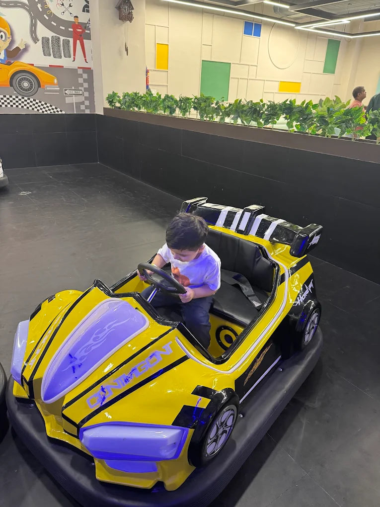 A young child drives a yellow bumper car in an indoor play area.