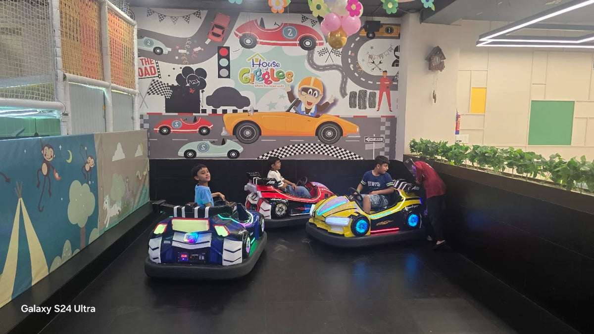 Children ride in bumper cars in an indoor play area with a race car-themed mural.