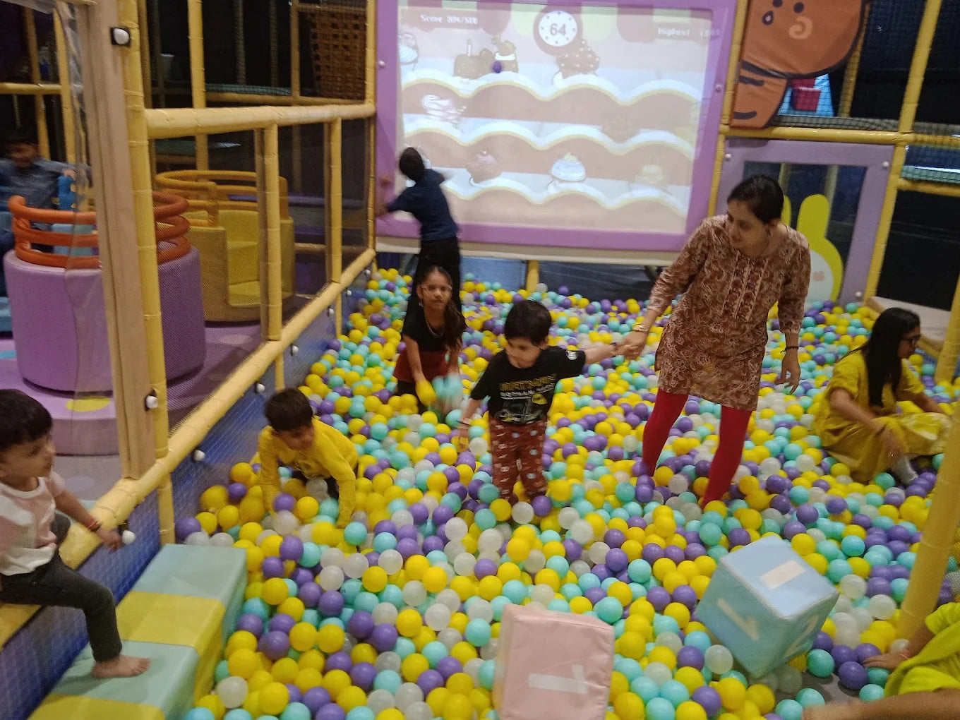 Children and adults play in a ball pit at an indoor playground.