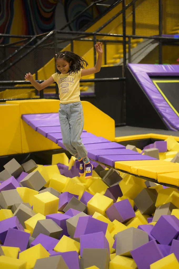 A young girl jumps in the air over a foam pit at a trampoline park.