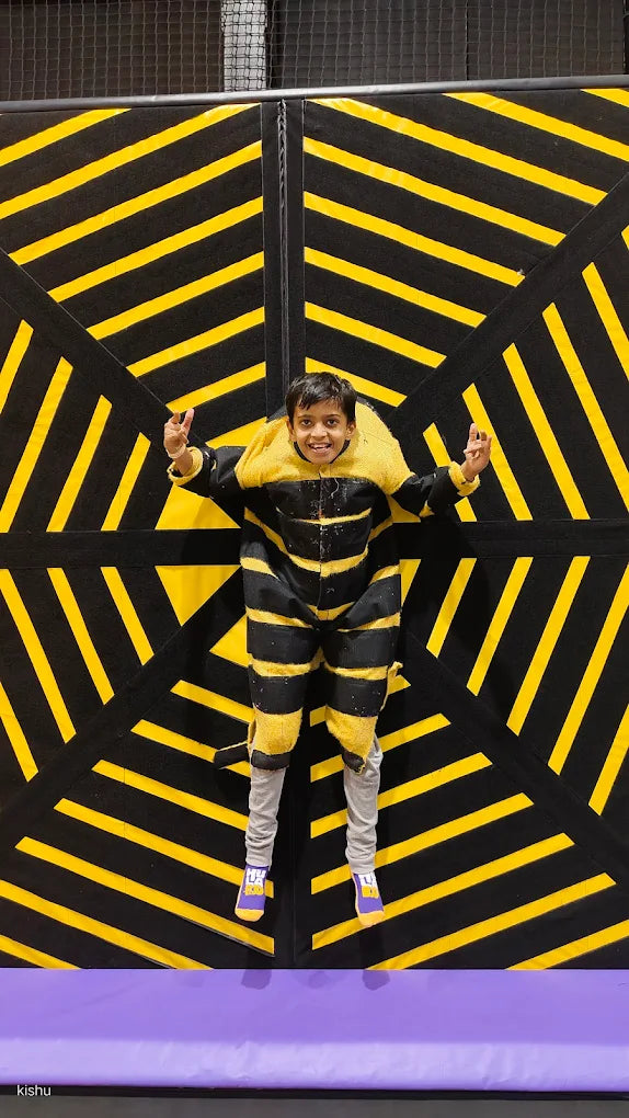 A child in a bee costume jumps against a black and yellow striped wall.