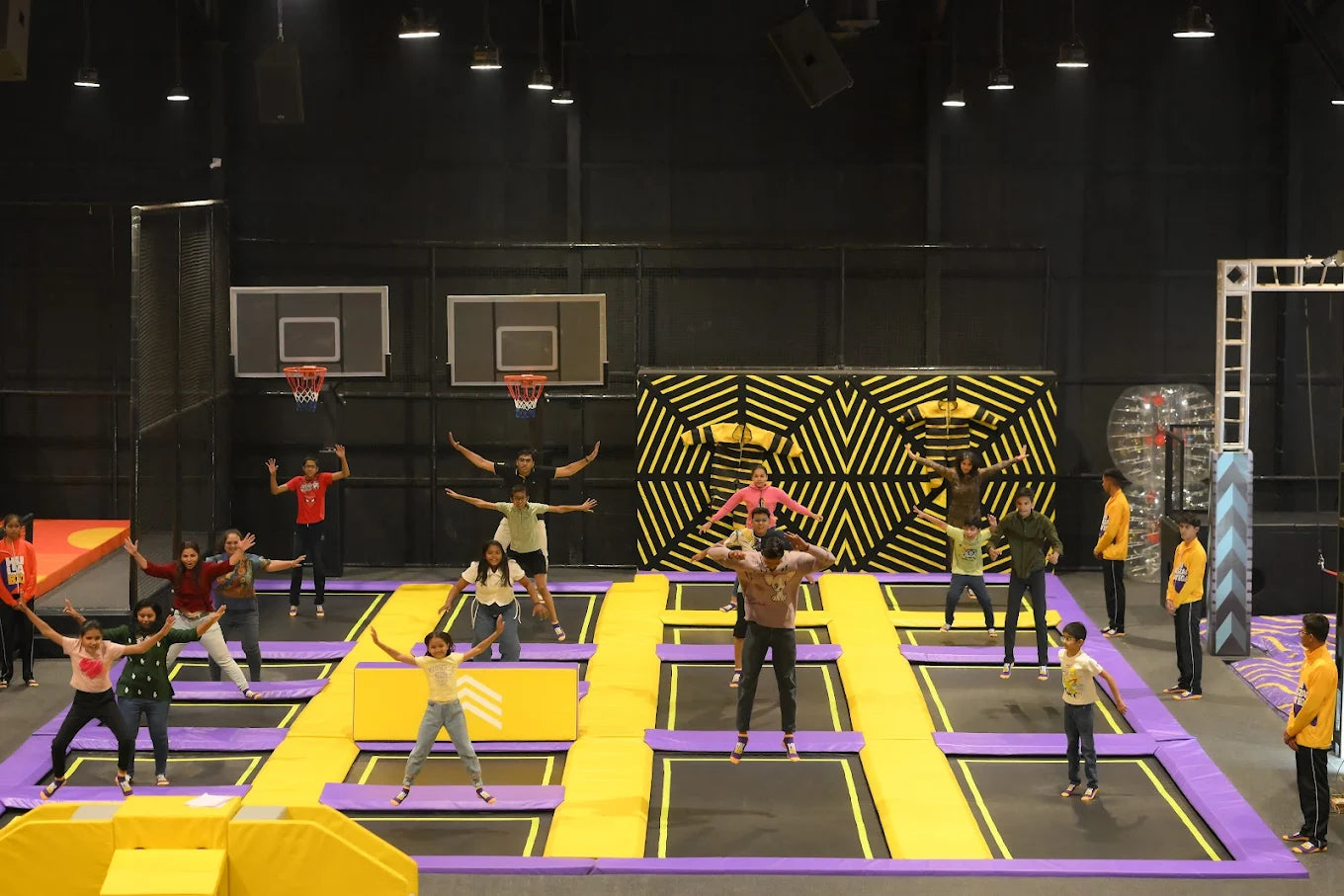 A group of young people jump and pose on trampolines in an indoor trampoline park.