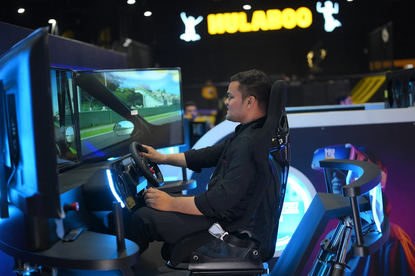 A young man plays a racing simulator game, gripping the steering wheel in a dark room with neon blue lights.